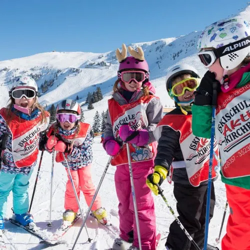 Kinder einer Skikursgruppe mit Helmen und Skibrillen auf der Piste